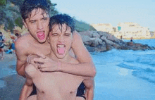 two young men are playing on the beach and one of them is holding the other on his back .