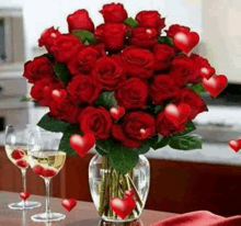 a vase filled with red roses and hearts is on a table next to wine glasses .