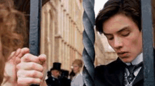 a man in a suit and tie is behind a fence holding onto a metal bar .