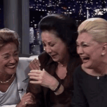 three women are sitting next to each other on a couch laughing .