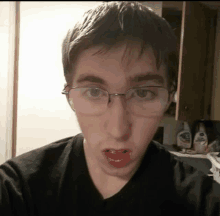 a young man wearing glasses and a black shirt is making a funny face .