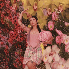 a woman in a pink dress is standing in front of a wall of flowers