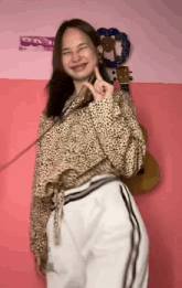 a girl in a leopard print shirt and white pants is dancing in front of a guitar