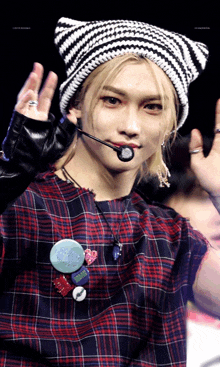 a young man wearing a plaid shirt and a striped beanie holds a microphone