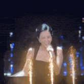 a woman is singing into a microphone in front of fireworks