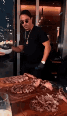 a man wearing sunglasses and a necklace is standing in front of a table with a plate of food .