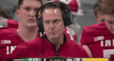 a man wearing headphones stands in front of a group of football players wearing red jerseys that say big
