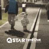 a man and a child are walking down a sidewalk with a star tamil chat logo on the bottom
