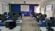 a classroom with lots of computer monitors and a projector on the ceiling