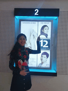 a woman holds a popcorn box in front of a sign that says 12