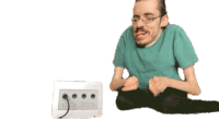 a man in a green shirt is sitting next to a nintendo gamecube controller