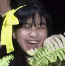 a young girl with a yellow bow on her head is smiling while holding a plant .