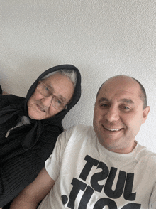 a man wearing a t2ul t-shirt poses with an older woman