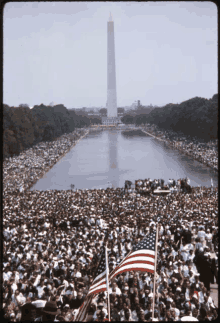 a large crowd of people gathered in front of a large body of water with the washington monument in the background