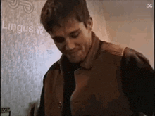 a man wearing a brown leather vest is standing in front of a wall .