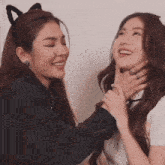 a woman wearing a cat ear headband holds another woman 's neck