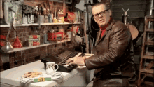 a man in a leather jacket is playing a keyboard in a garage with a bag of evergreen tea on the shelf behind him