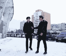 two men are standing in the snow in front of a row of buses .