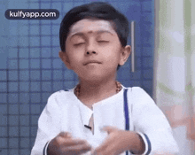 a young boy is making a funny face with his eyes closed and his hands folded .