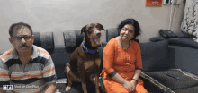 a man and a woman are sitting on a couch with a dog in front of them