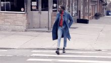 a man in a blue coat is crossing a street in front of a building that has the word taxi on it