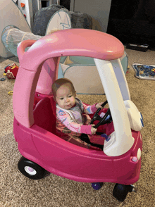 a baby is sitting in a pink toy car with a steering wheel