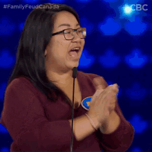 a woman wearing glasses applauds in front of a microphone while wearing a name tag that says " ter " on it