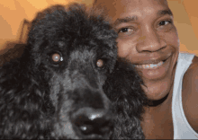 a man in a white tank top is smiling while holding a black poodle