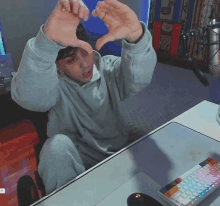 a man sitting at a desk making a heart shape with his fingers