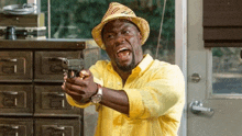 a man wearing a hat and a yellow shirt is pointing a gun