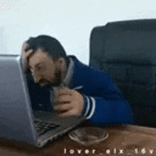 a man is sitting at a desk in front of a laptop computer holding his head .