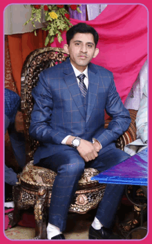 a man in a suit sits in a chair with his hands folded