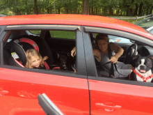 a woman sits in a red car with two dogs