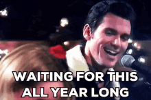 a man singing into a microphone with the words " waiting for this all year long " written below him .