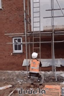 a construction worker is kneeling down in front of a brick building while wearing a hard hat and an orange vest .