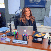 a woman sits at a desk with an apple laptop and a name plate that says capt. olivia benson