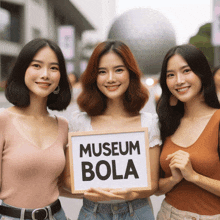 three women hold a sign that says museum bola