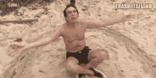 a shirtless man is sitting in the sand with his arms outstretched .