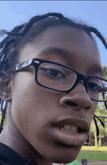 a young man wearing glasses looks at the camera with a blue sky behind him