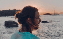 a man with long hair and a beard looks out over a body of water at sunset