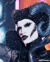 a drag queen is wearing a black and white costume with horns and rhinestones .