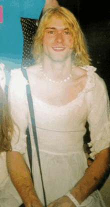 a man with blonde hair is wearing a white dress and a necklace