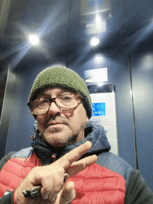 a man wearing a green hat and glasses giving the peace sign in an elevator