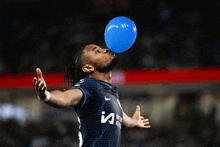 a soccer player blowing up a blue balloon with the letter i on his shirt