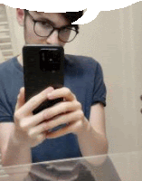 a man wearing glasses is taking a picture of himself in the mirror .