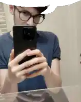 a man wearing glasses is taking a picture of himself in the mirror .