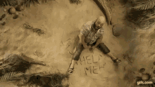 a man is sitting in the sand with the words `` help me '' written on the sand .