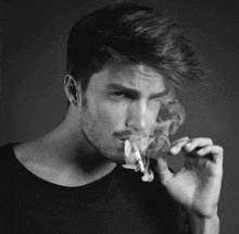 a black and white photo of a man smoking a cigarette in a black shirt .