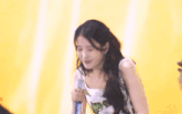 a woman is holding a microphone in front of a yellow curtain and smiling .