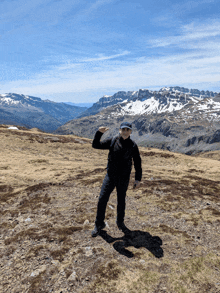 a man stands on top of a grassy hill with snowy mountains in the background